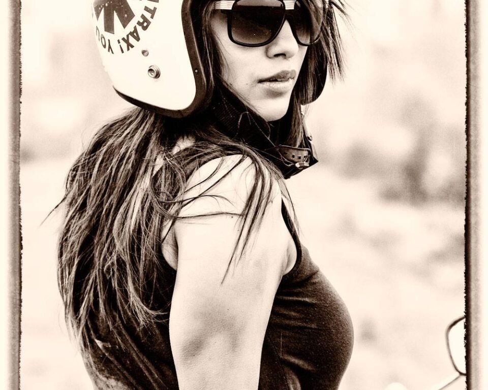 Sepia-toned editorial fashion portrait by AHSANZ featuring a stylish woman in a vintage motorcycle helmet and large sunglasses, looking over her shoulder.