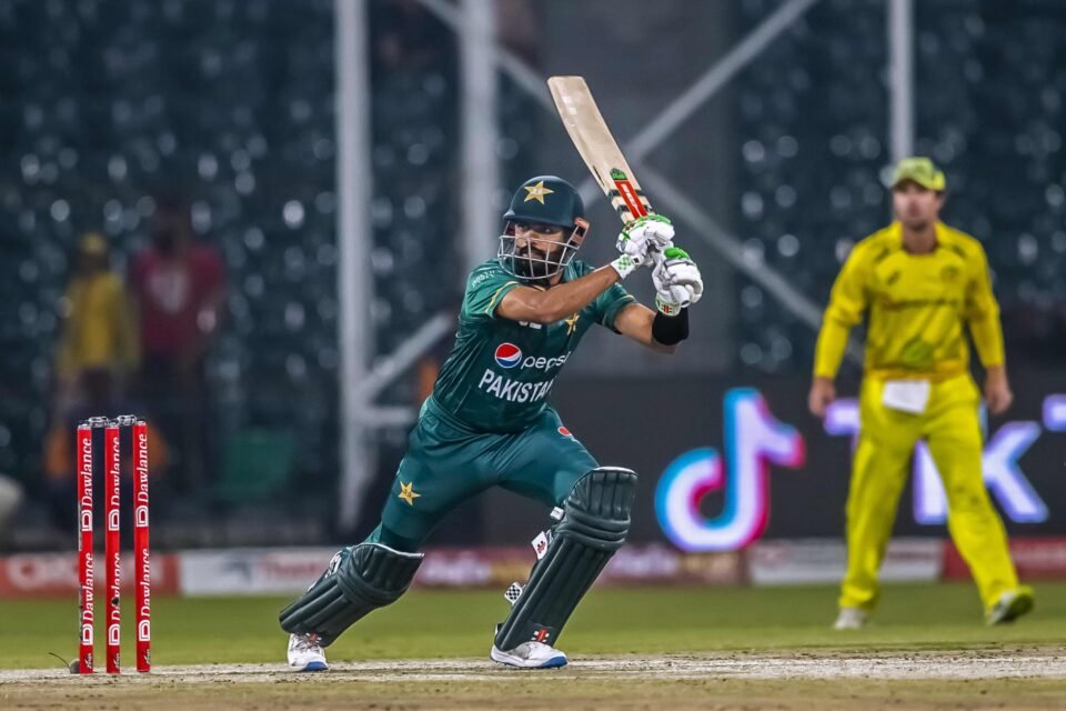 Professional photograph of a Pakistani cricket batsman mid-stroke, focusing on the intense action under stadium lights with the stumps visible. Sports action photography by AHSANZ.