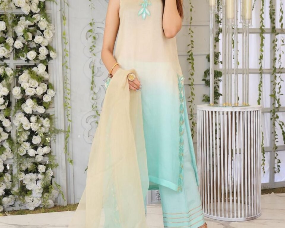 Full-length editorial fashion photograph of a model standing in a white, ornate room, wearing a sleeveless cream and ombre aqua blue traditional Pakistani suit with silk trousers and a sheer dupatta. Fashion photography by AHSANZ.