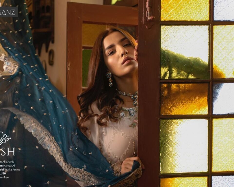 Close-up editorial fashion portrait for the LUSH campaign featuring model Hafsa Janjua leaning out from behind an antique wooden doorway with yellow stained glass, wearing a light embroidered outfit and blue dupatta. Fashion and jewelry photography by AHSANZ.