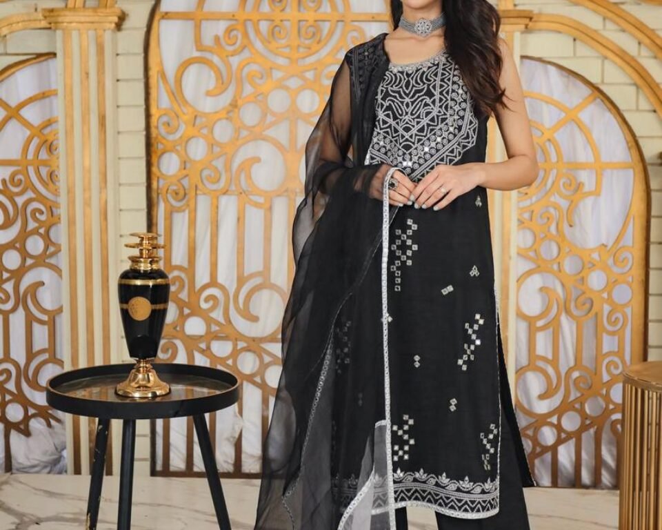 Editorial fashion portrait of a model standing in a white and gold ornate room, wearing a sleeveless black traditional Pakistani suit with heavy silver embroidery, draped with a sheer black and silver dupatta. Fashion and jewelry photography by AHSANZ.
