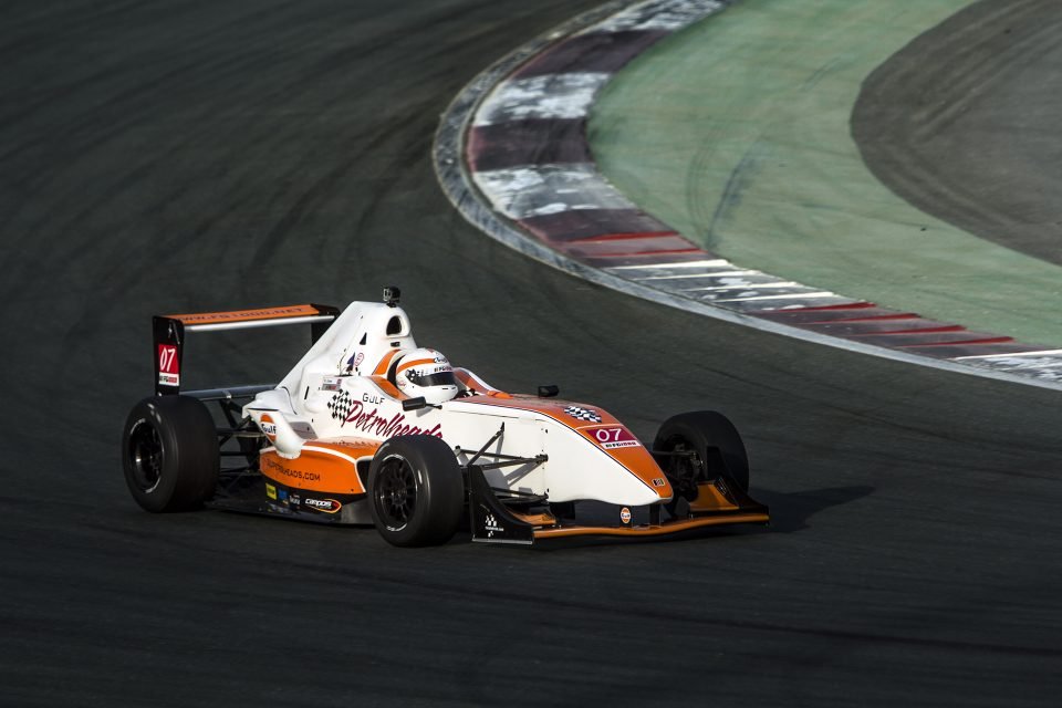 Professional photograph of a white and orange formula racing car with the number 07 cornering sharply on a circuit track. High-speed action photography by AHSANZ.